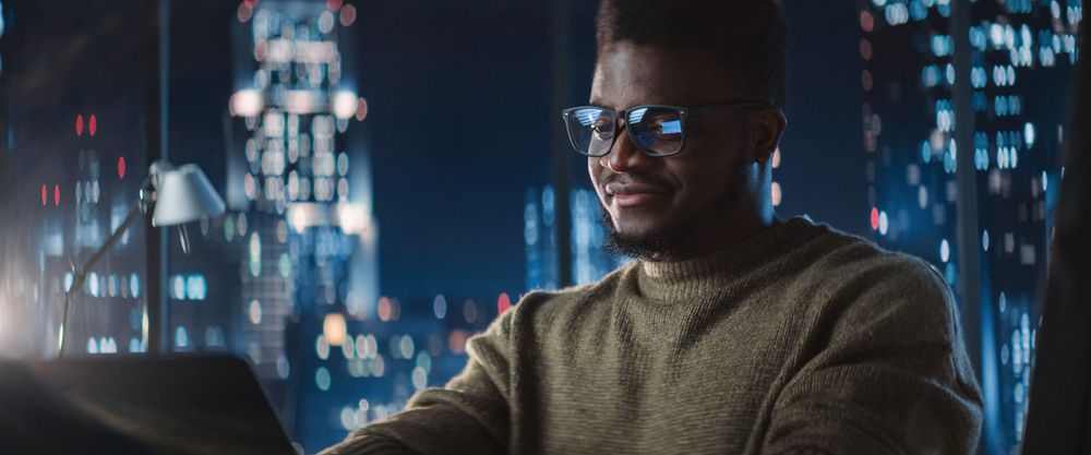 Successful Black Businessman Working on Laptop Computer in Big City Office Late at Night.
