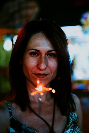 Woman holding sparkler on fairground in evening