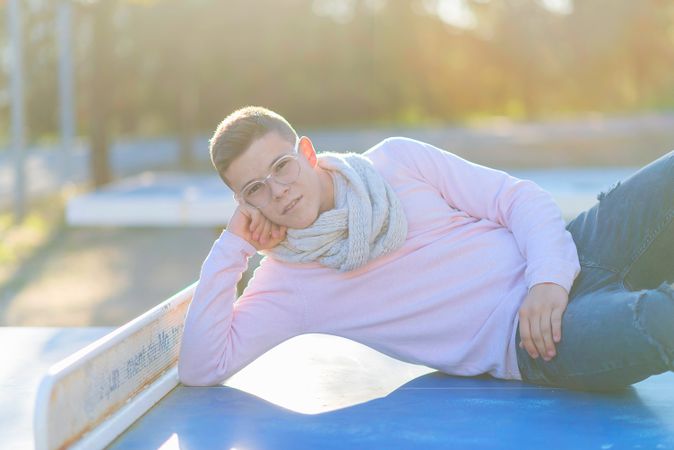 Smiling teenage male in striking eyewear leaning on ledge in a city park