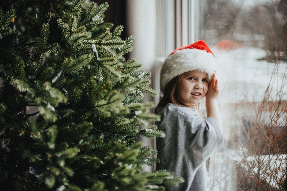 Girl in Christmas hat standing beside green Christmas tree