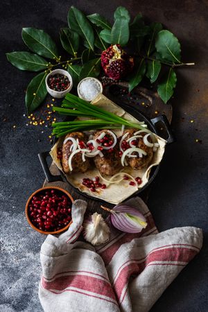 Looking down at Georgian plate of abkhazura meat cutlets with pomegranate seeds, bay leaves & onions