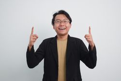 Joyful Asian businessman with suit and casual shirt pointing up