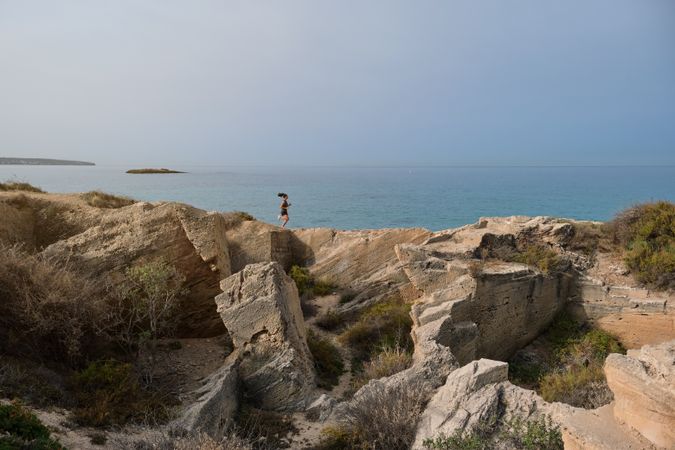 Woman running on rocky cliff near sea
