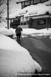Back view of older person walking in snow-covered neighborhood in grayscale 0yGEq4