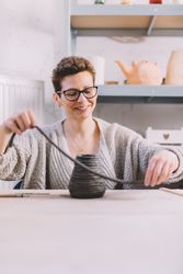 Adult woman putting clay roll on unfinished pot