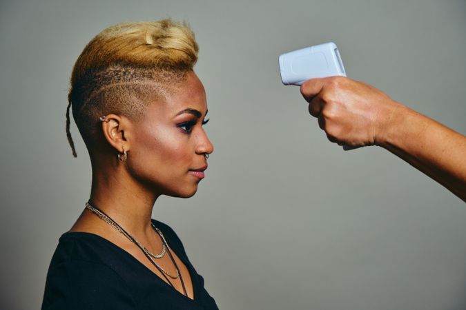 Black woman with short blonde hair having her temperature checked