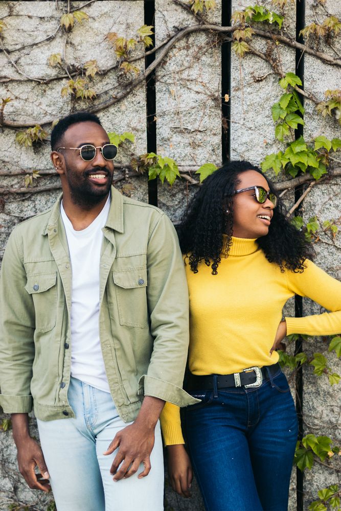 Black couple posing in front of wall with foliage