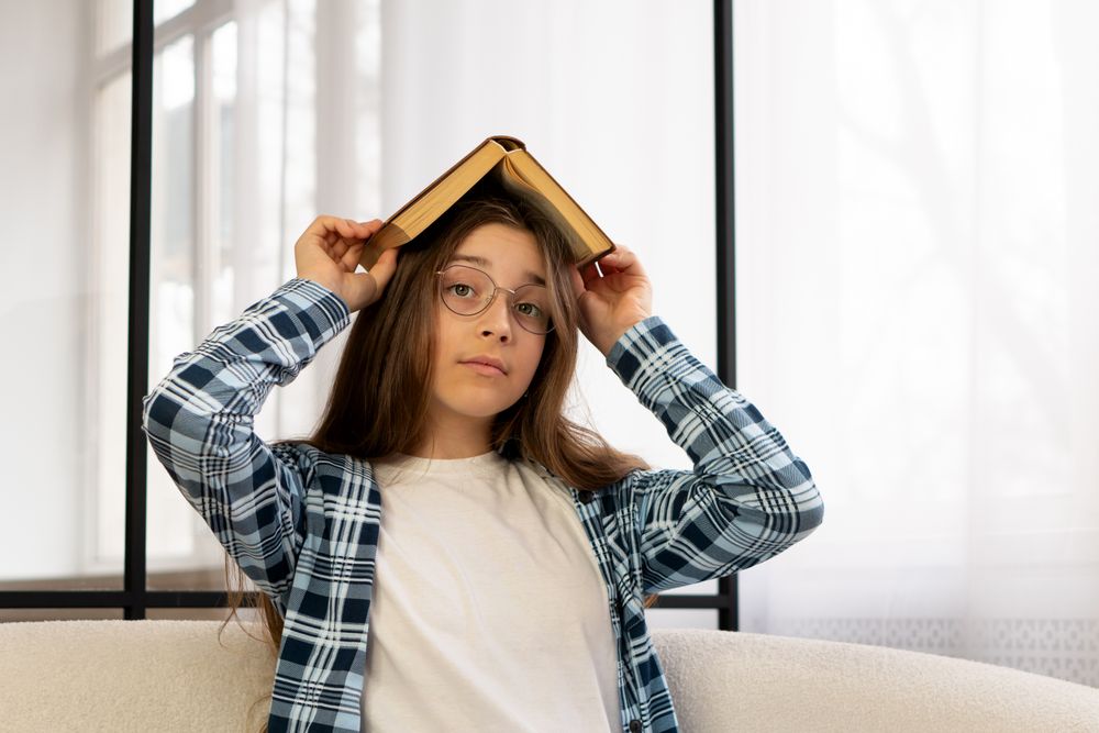 Girl holding book over head sitting on sofa indoors.