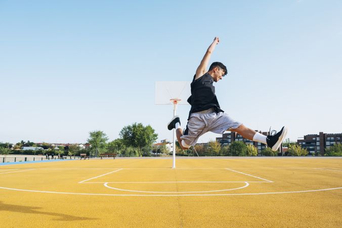 Young man playing on yellow basketball court outdoor jumping happily