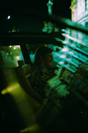 Side view of smiling young man sitting on driver seat of an old car at night