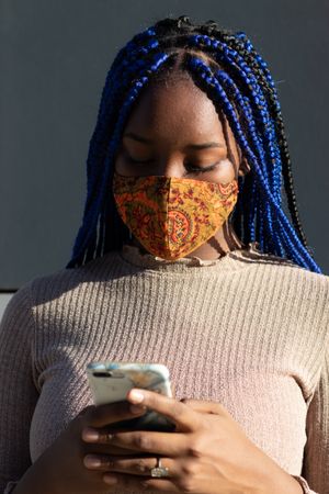 Black woman in mask messaging on smartphone in city