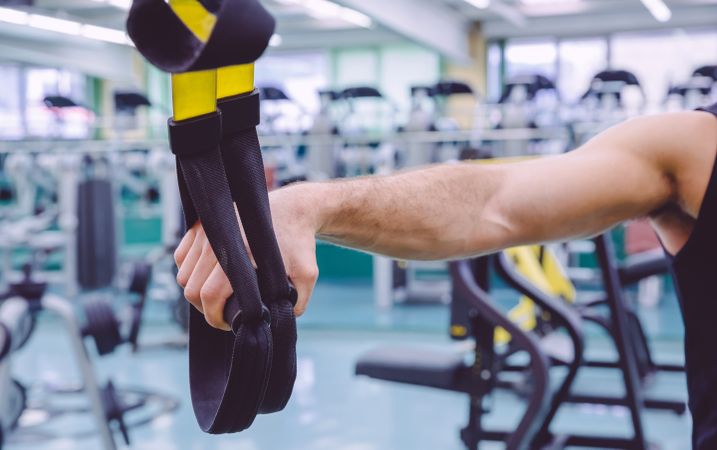 Arm of man holding suspension ropes in gym