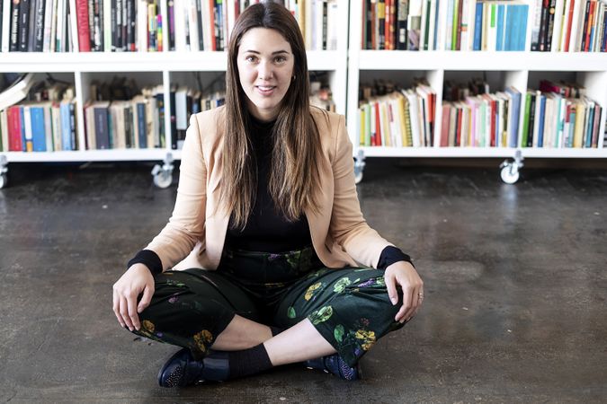 Portrait of a surprised woman sitting cross legged in front of book shelf