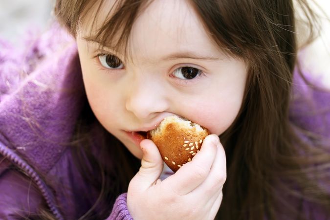 Portrait of a girl with Down syndrome eating bread