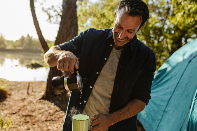 Smiling mature man pouring coffee from kettle into a cup