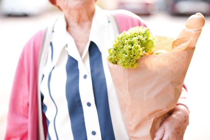 Older woman in pink cardigan holding grocery bag standing in close-up