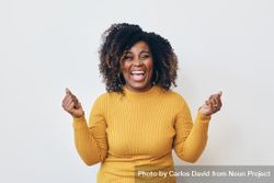Studio shot of a excited Black woman in yellow shirt celebrating beGPl5