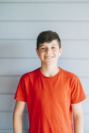 Portrait of a cheerful male teen leaning on wood wall while looking camera