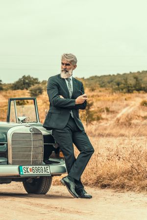 Man in suit leaning on car and looking away in desert