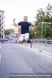 Young blonde male jumping outdoors while looking camera in the street 5wXp1y