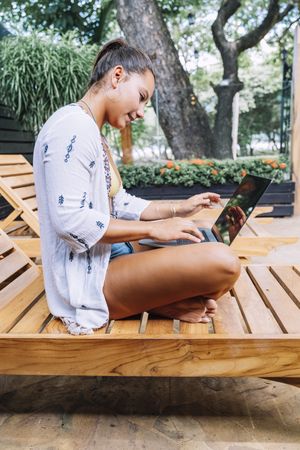 Relaxed woman using laptop while resting on deck chair