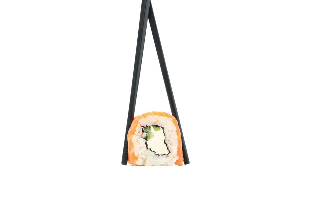 Chopsticks with sushi roll isolated on plain background