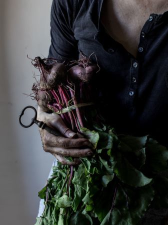 Faceless person with bunch of beetroots and key