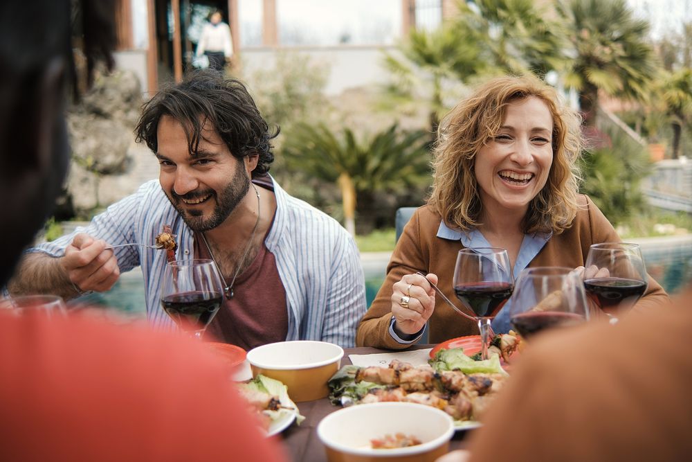 A group of friends are enjoying a meal together at a picnic table set in the countryside