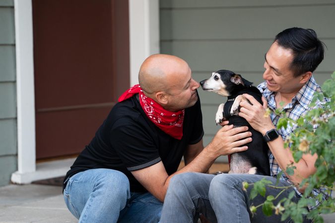 Man holding his dog and his partner leaning in giving the pet affection