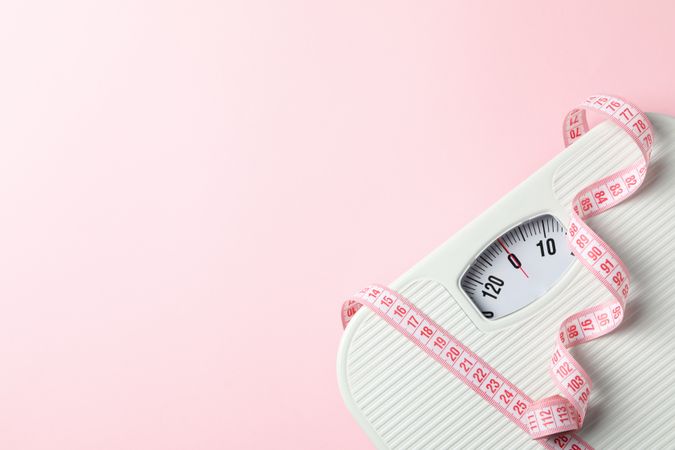 Scales and measuring tape on pink background. Weight loss concept
