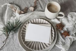 Blank card, invitation mockup on ceramic plate with pine branch and cookies on tablecloth