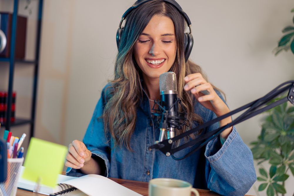 Happy young female podcaster enjoying creative content recording session with professional audio equipment in home studio