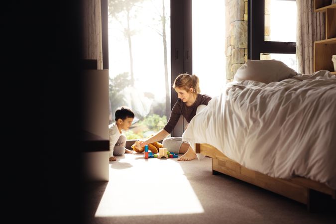 Mother and little son are playing with different developing toys in bedroom