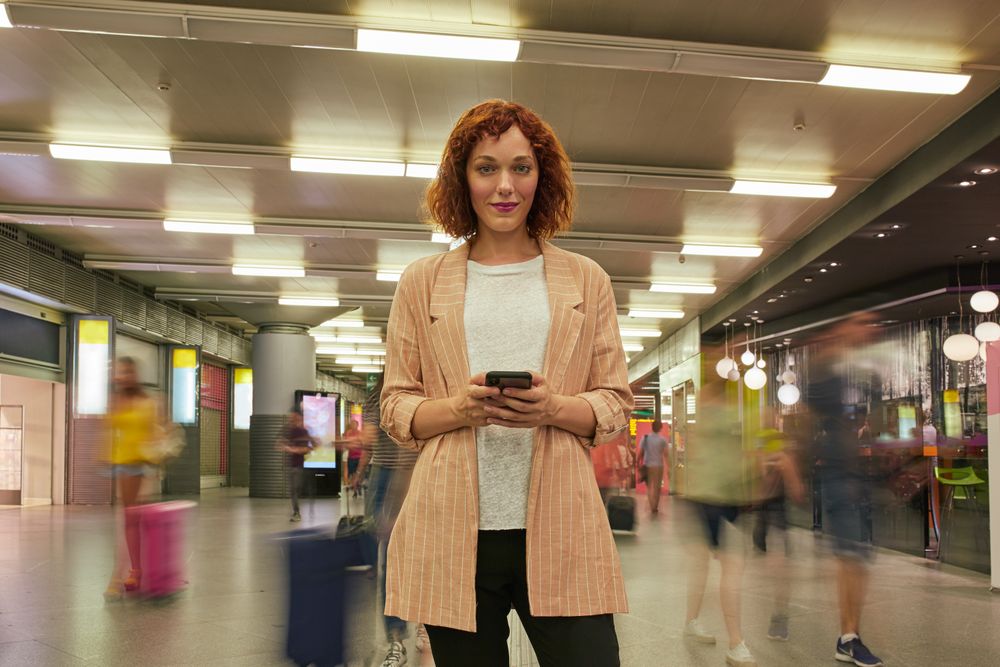 Red haired young woman using smartphone at station