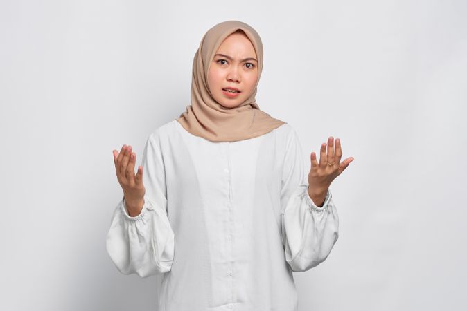 Stern Muslim woman in headscarf in light blouse with hands up in a questioning way