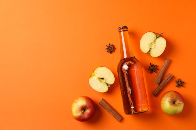 Composition with cider, apples and cinnamon on orange background