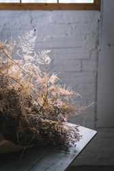 Bunch of plant in paper on table near stool in grey room