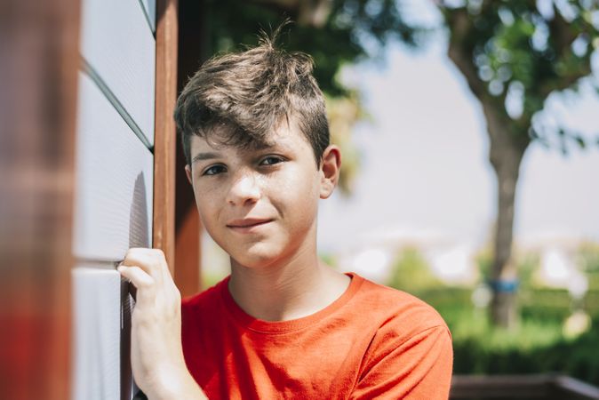 Portrait of a cheerful male teen leaning on wood wall outside while looking camera