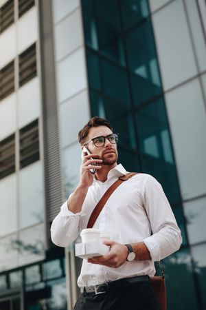 Man carrying two coffee cups in hand talking on mobile phone going to office in the morning