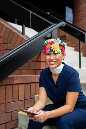 Nurse sits outside of hospital on stairs taking a break smiling and looking at camera