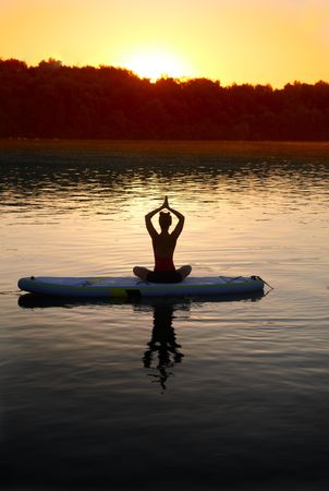 Woman sitting cross legs on paddle board in the middle of a lake at dusk