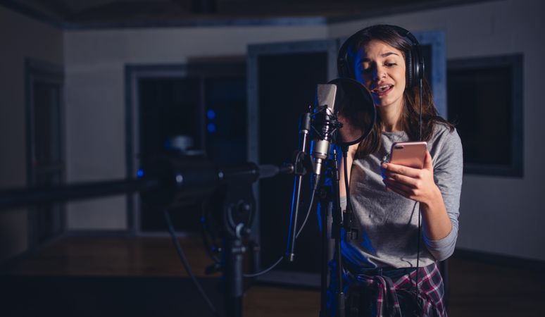 Female playback singer with microphone and reading lyrics from her mobile phone