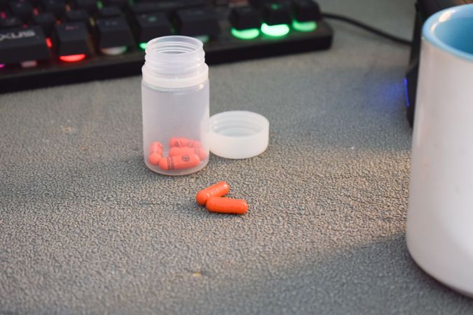 Red pills in container on desk in front of keyboard
