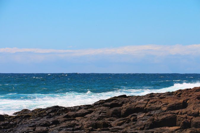 Clear sky and rolling waves create a tranquil coastal view with rocky shoreline at midday