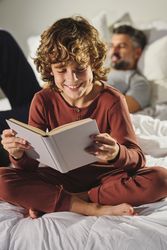 Child reading book on bed against father