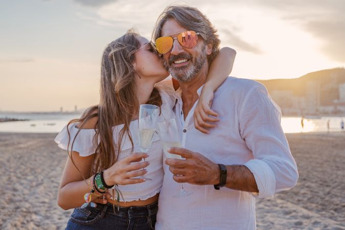 Father kissing daughter and clinking glasses on beach