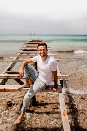 Content male relaxing on old wooden pier on seashore