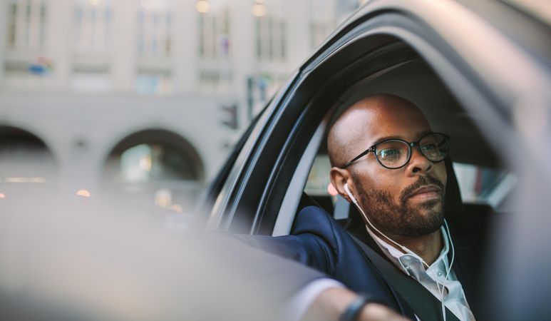 Businessman wearing earphones and listening musing while driving a car