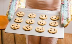 Woman holding a tray with baked cookies with kitchen gloves
