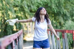 Smiling woman standing on foot bridge in forest with outstretched arms
